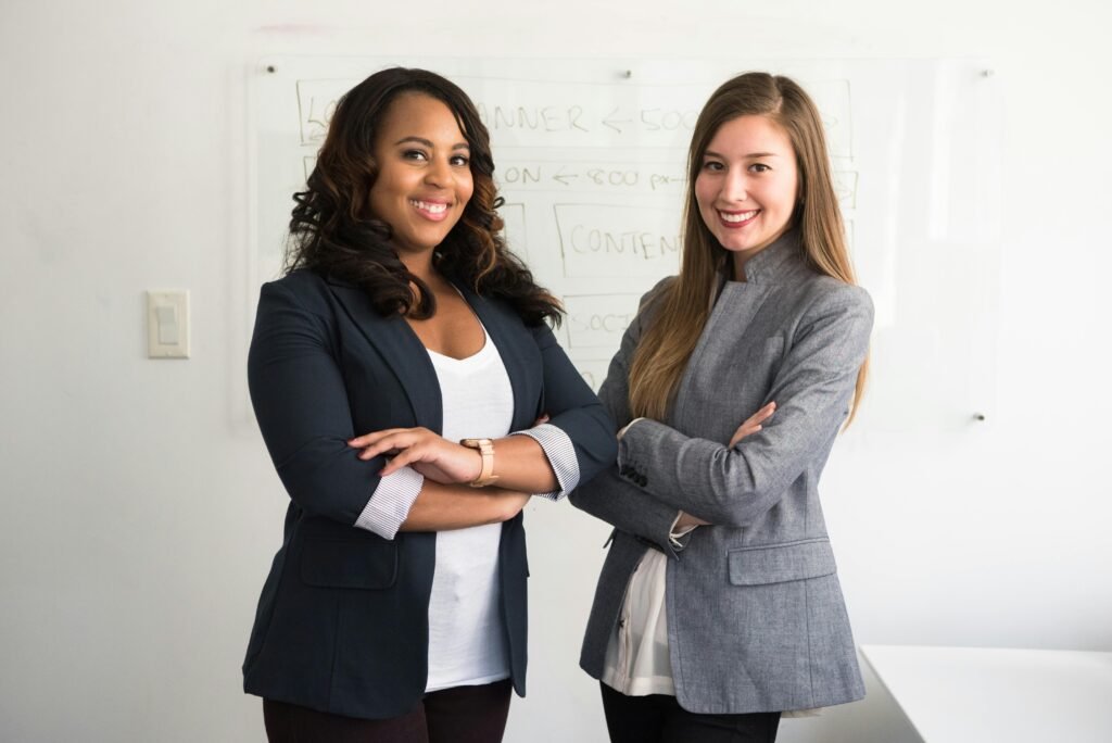 pexels-photo-1181527-1181527 Two diverse businesswomen smiling confidently in a modern office environment.