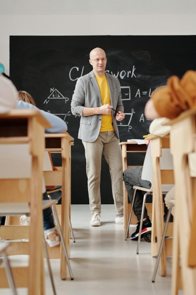 pexels-photo-5212339-5212339 Bald teacher explaining geometry on blackboard to attentive students in classroom.