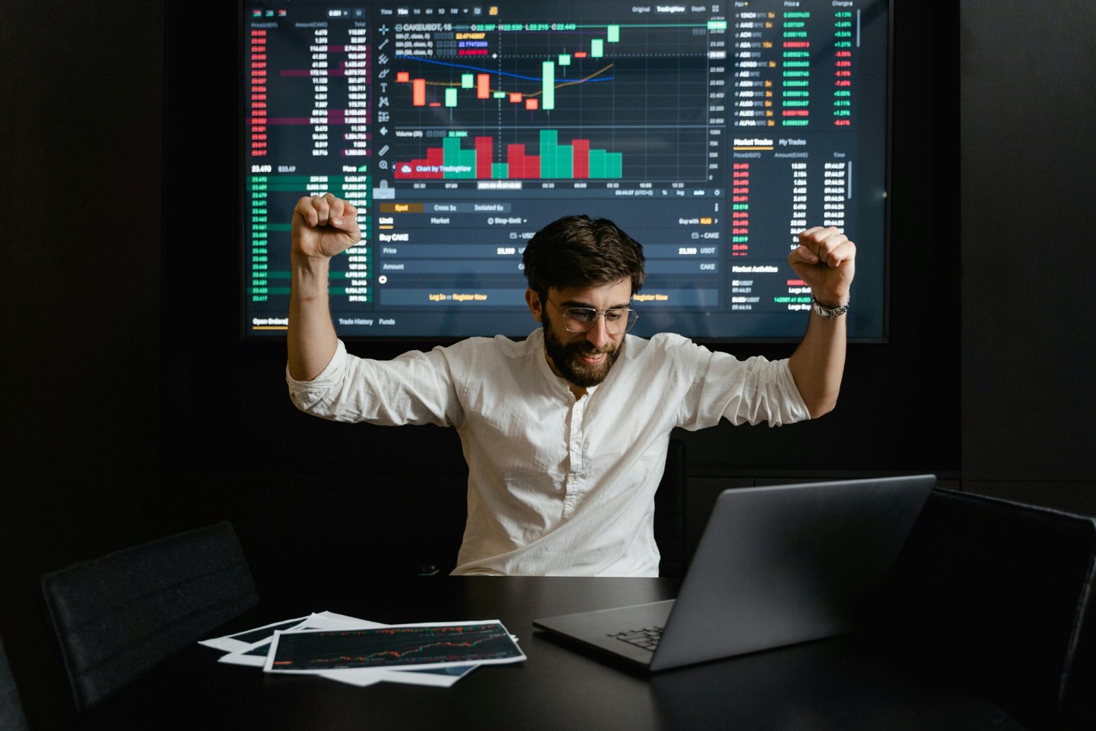 pexels-photo-7567565-7567565 Businessman celebrates stock market success with hands raised in excitement at a trading desk.